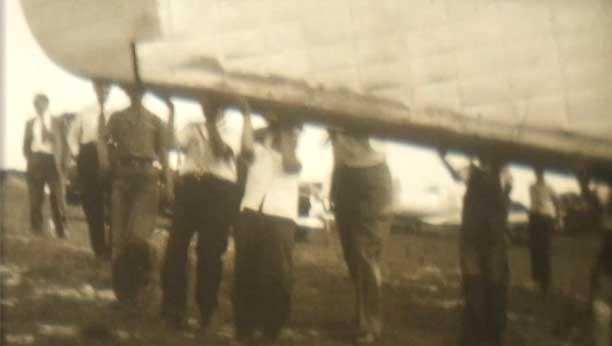 A dated image from the early 20th century of men holding up a row boat.