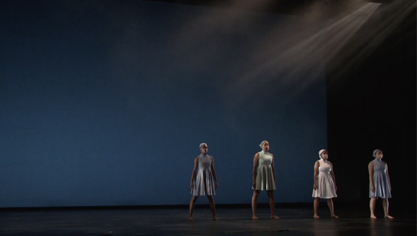 Image of four dancers on a dark stage.