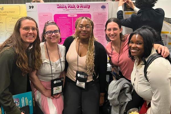 A group of five researchers from the women's center poses in front of their poster presentation