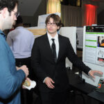 A young undergraduate researcher presenting his research to the public