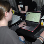 A young undergraduate researcher presenting her research to the public is playing a video game that was produced by members of the video game club
