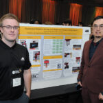 Two youn undergraduate student stand besde their reserach poster