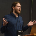A young undergraduate researcher presenting his research to the public