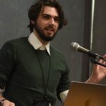 A young resreach at a podium explaining his research