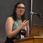 A young resreach at a podium explaining her research